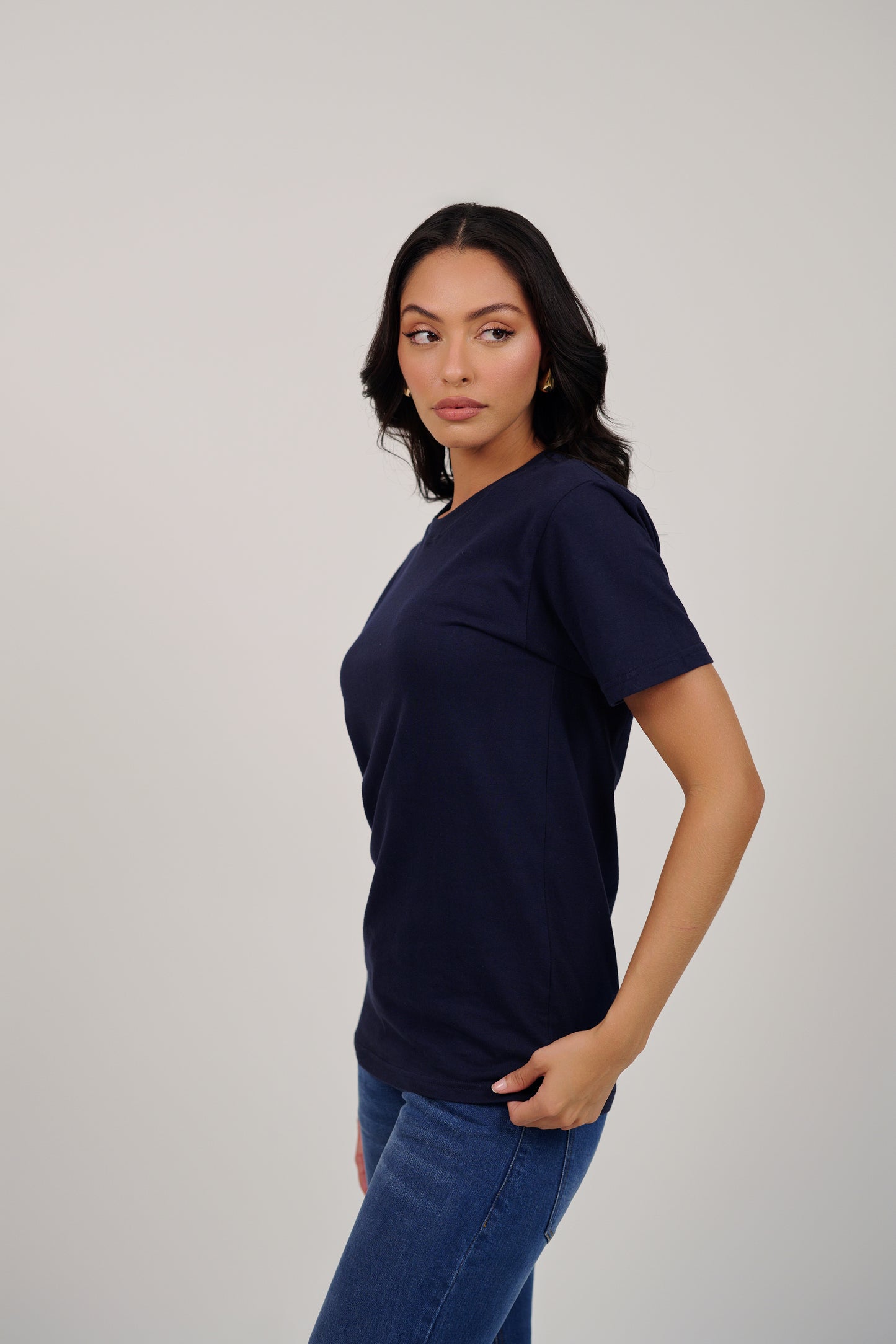 Woman wearing a navy blue t-shirt and jeans on a plain background