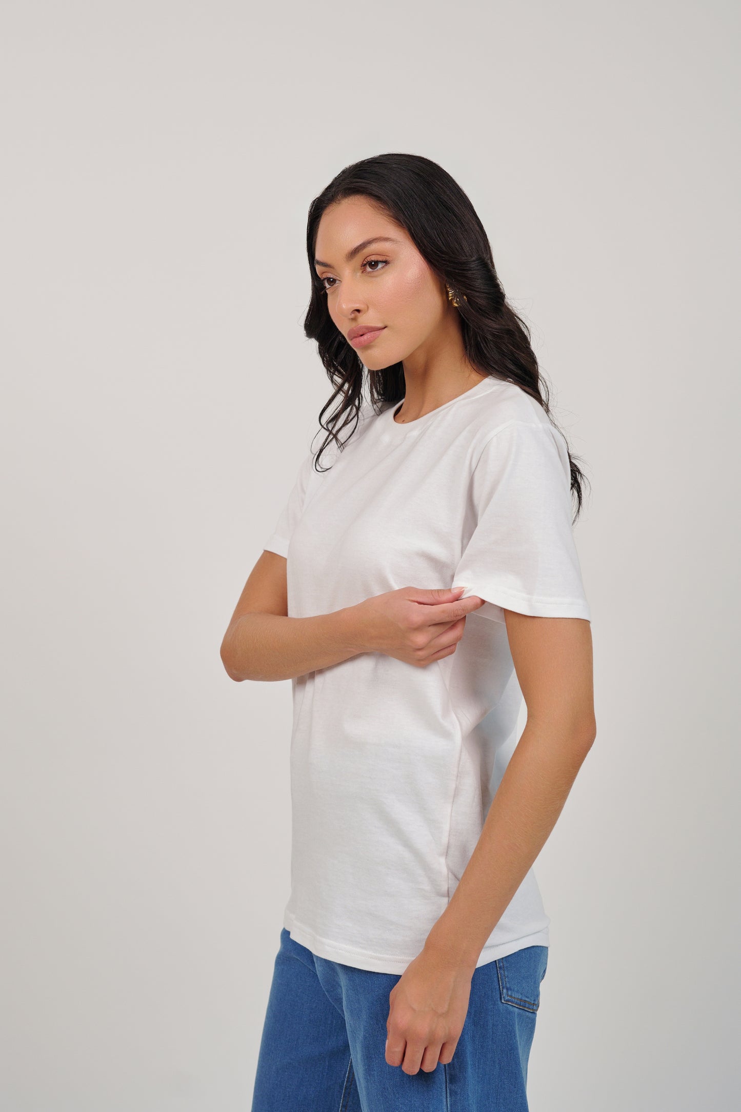 Woman wearing a plain white t-shirt and blue jeans against a light gray background