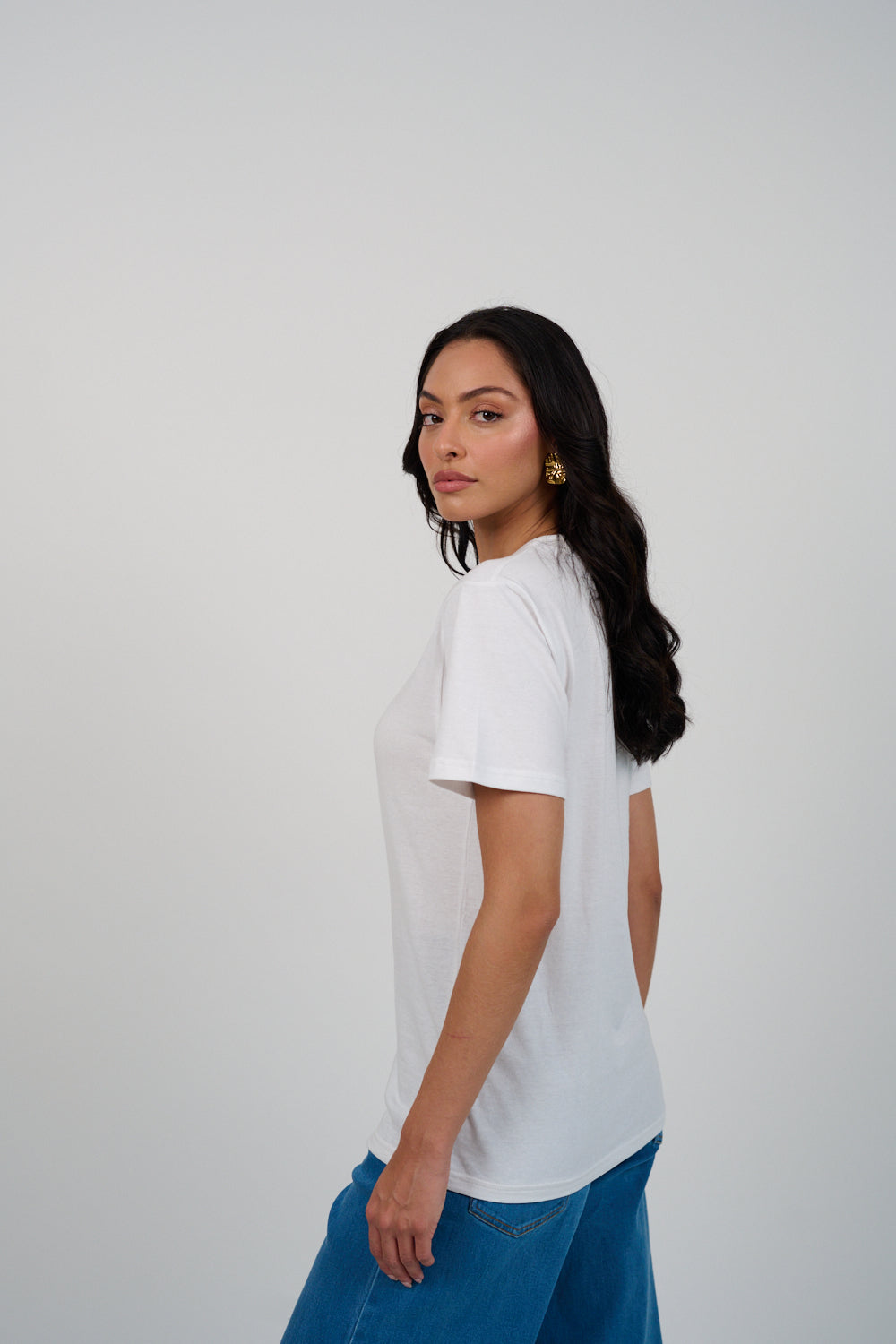 Woman wearing a white t-shirt and blue pants against a plain background