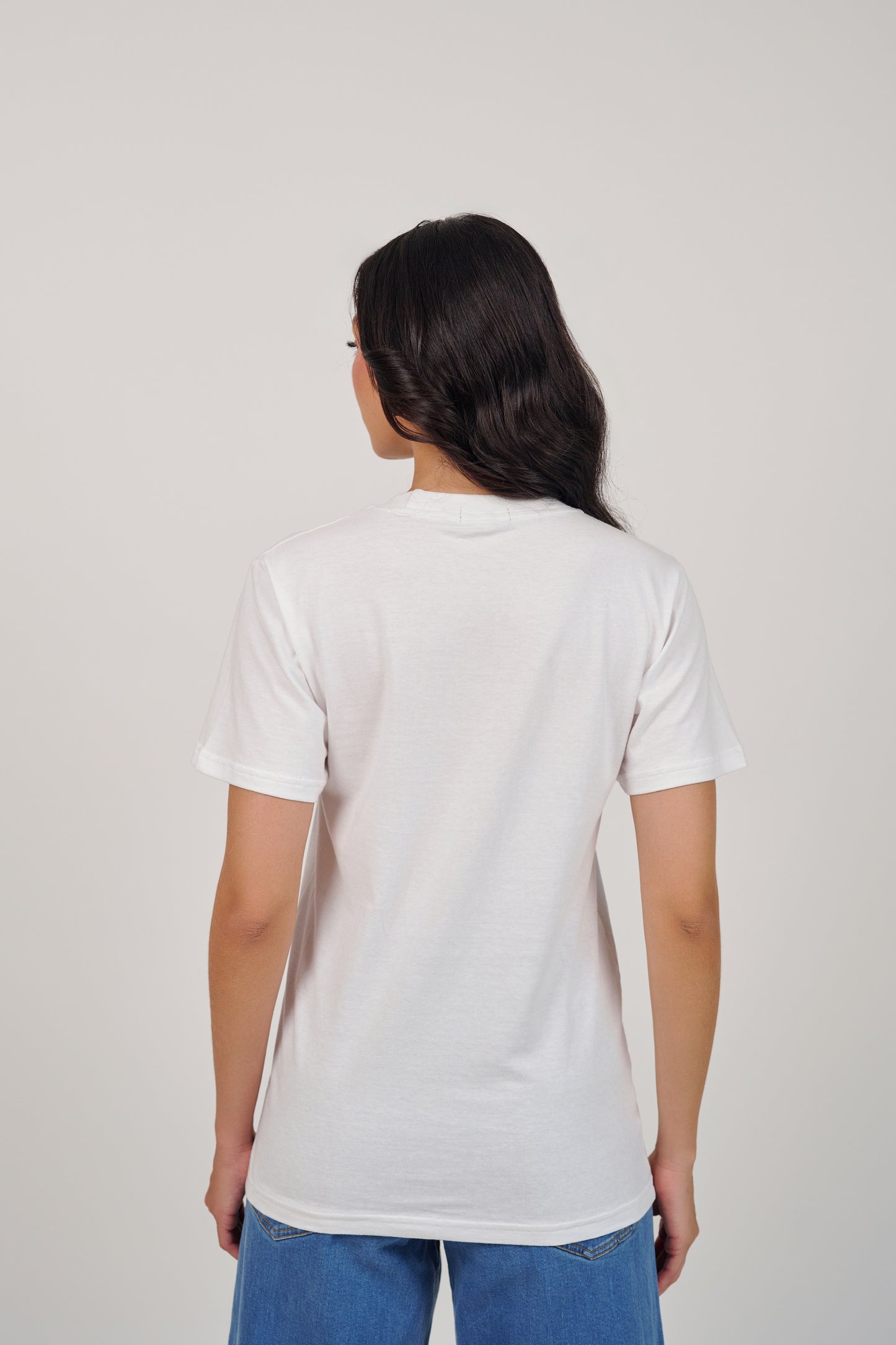 Person wearing a plain white t-shirt and blue jeans on a light gray background