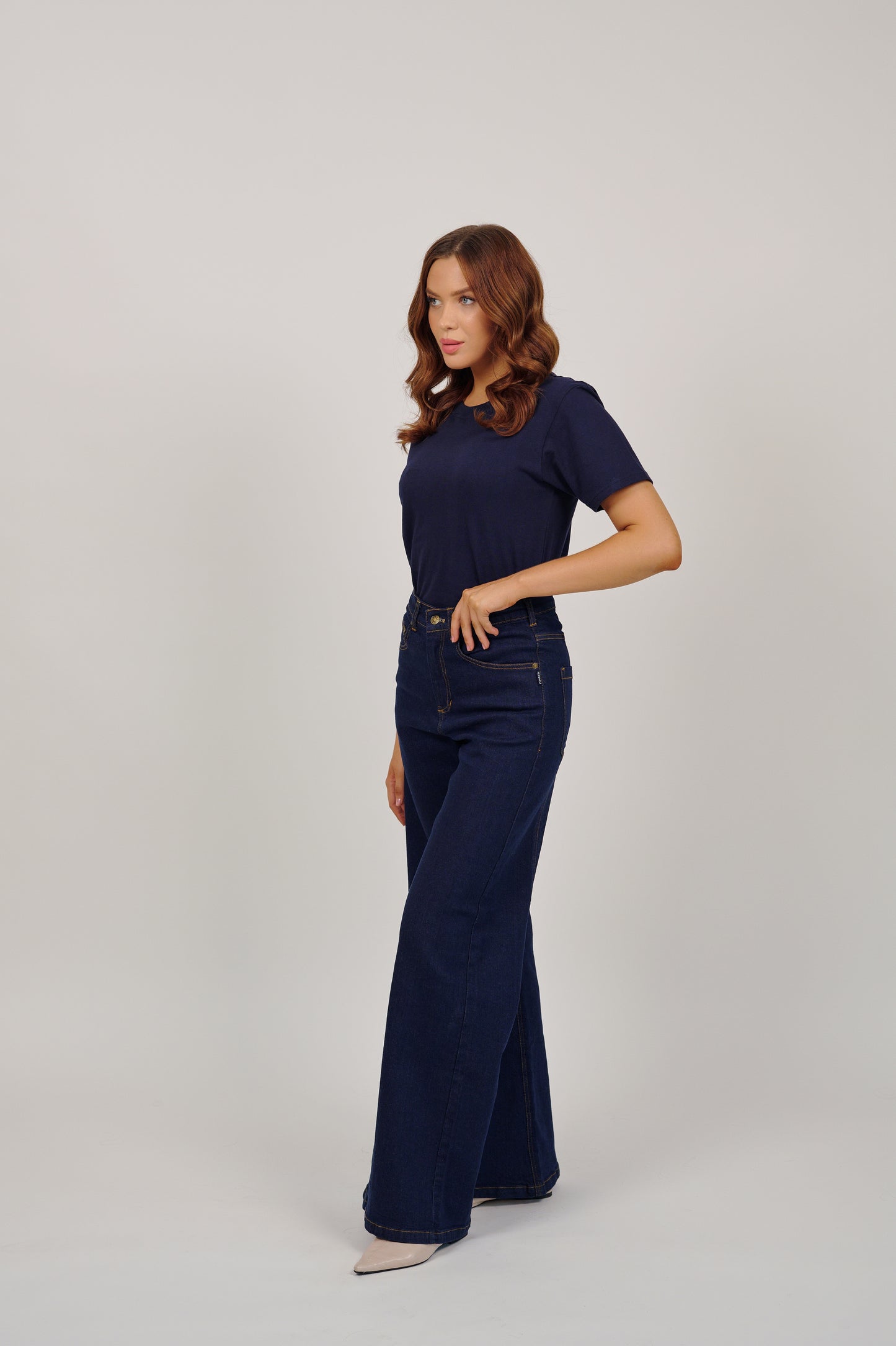 Woman wearing a navy blue top and wide-leg jeans on a light gray background