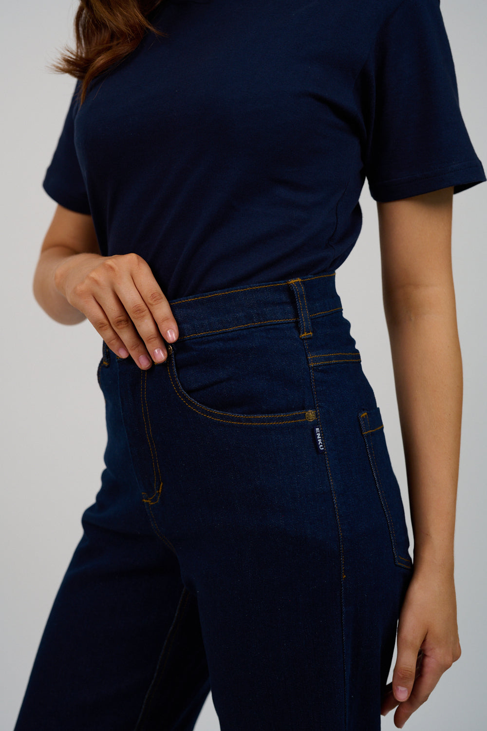 Person wearing a navy blue t-shirt and dark jeans on a plain background