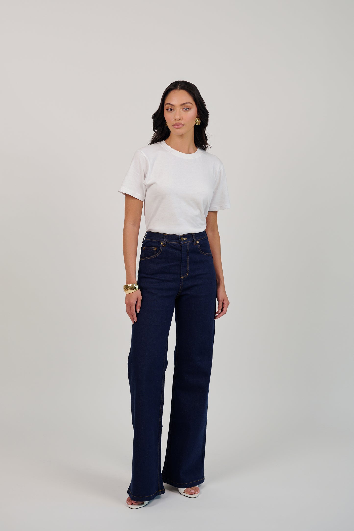 Woman wearing a white t-shirt and dark blue jeans on a plain background