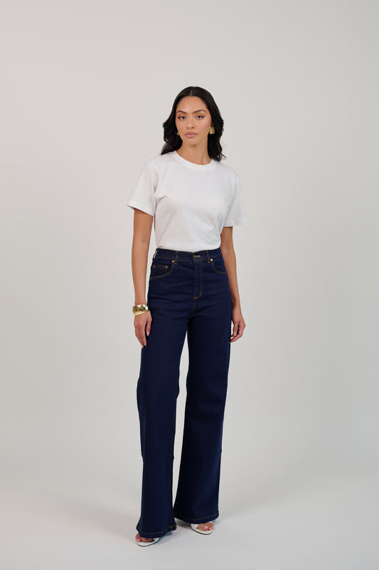 Woman wearing a white t-shirt and dark blue jeans on a plain background