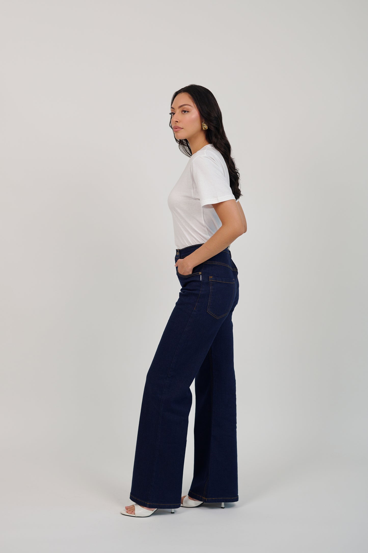 Woman wearing a white t-shirt and dark blue jeans on a plain background