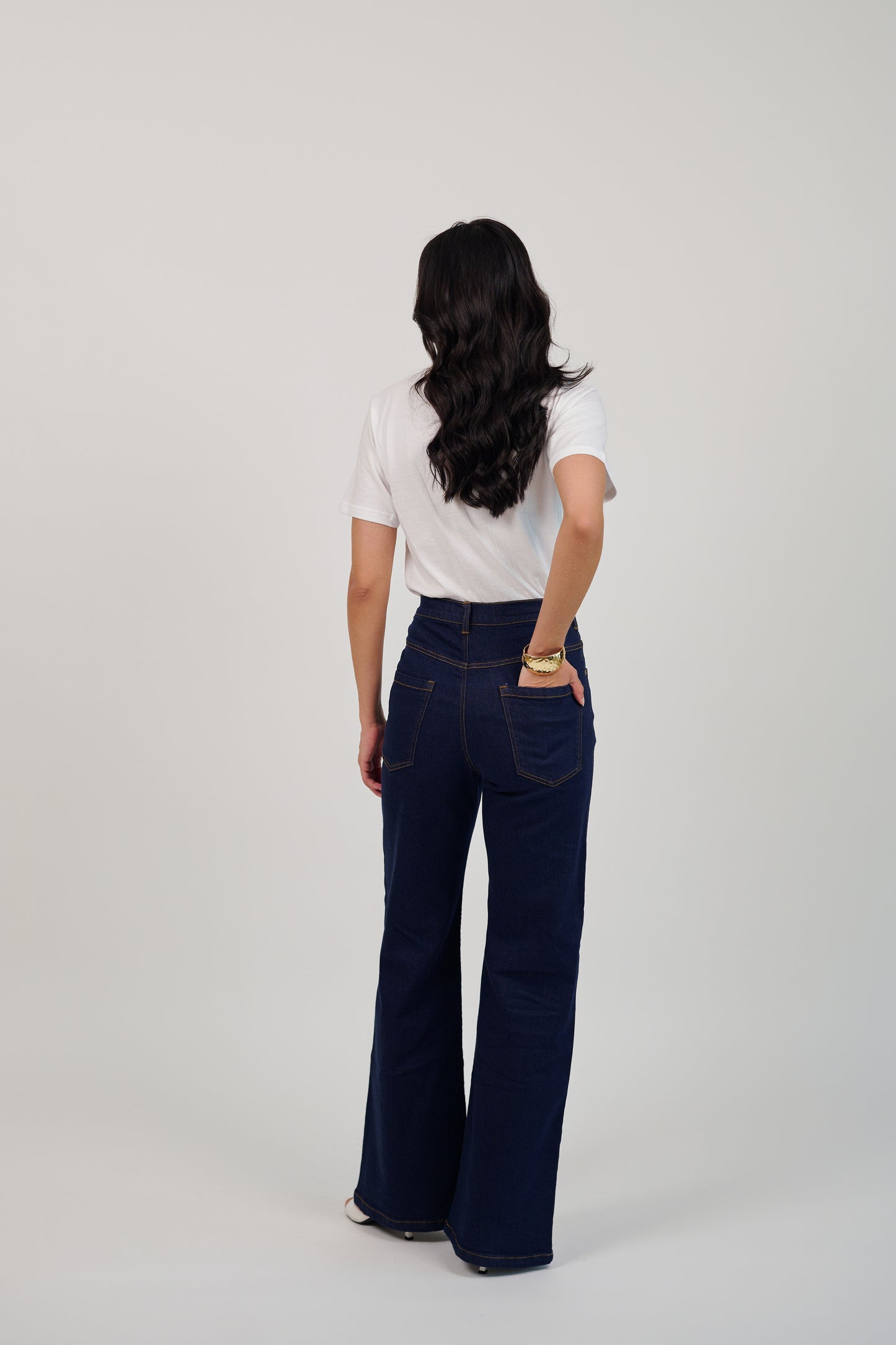Person wearing a white shirt and dark blue jeans on a plain background