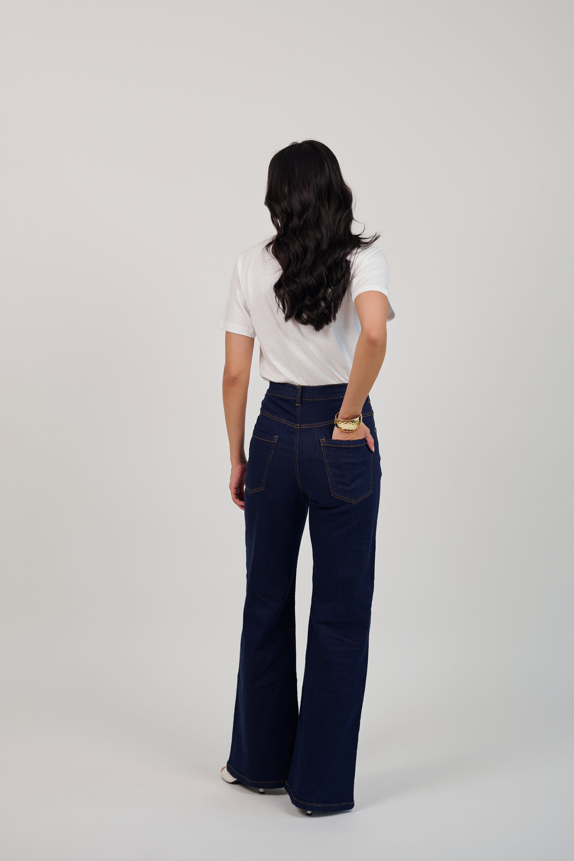 Person wearing a white shirt and dark blue jeans on a plain background