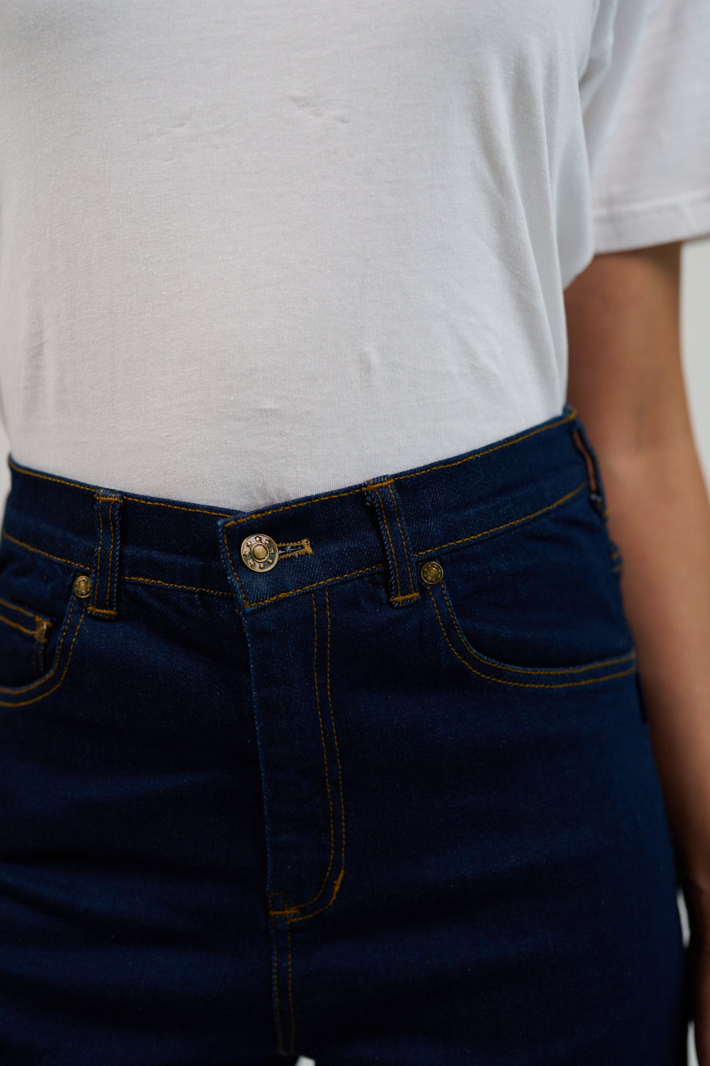 Person wearing a white t-shirt and dark blue jeans with a visible brand logo.