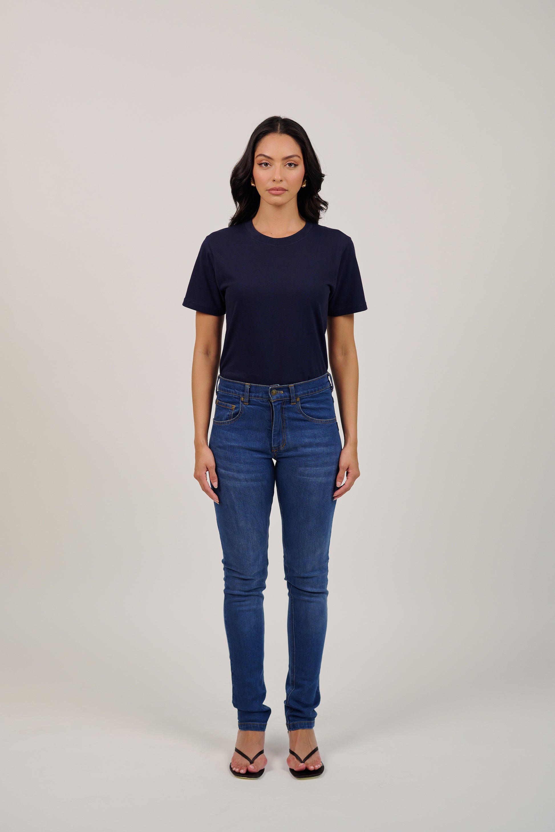 Woman wearing a navy t-shirt and blue jeans on a plain background