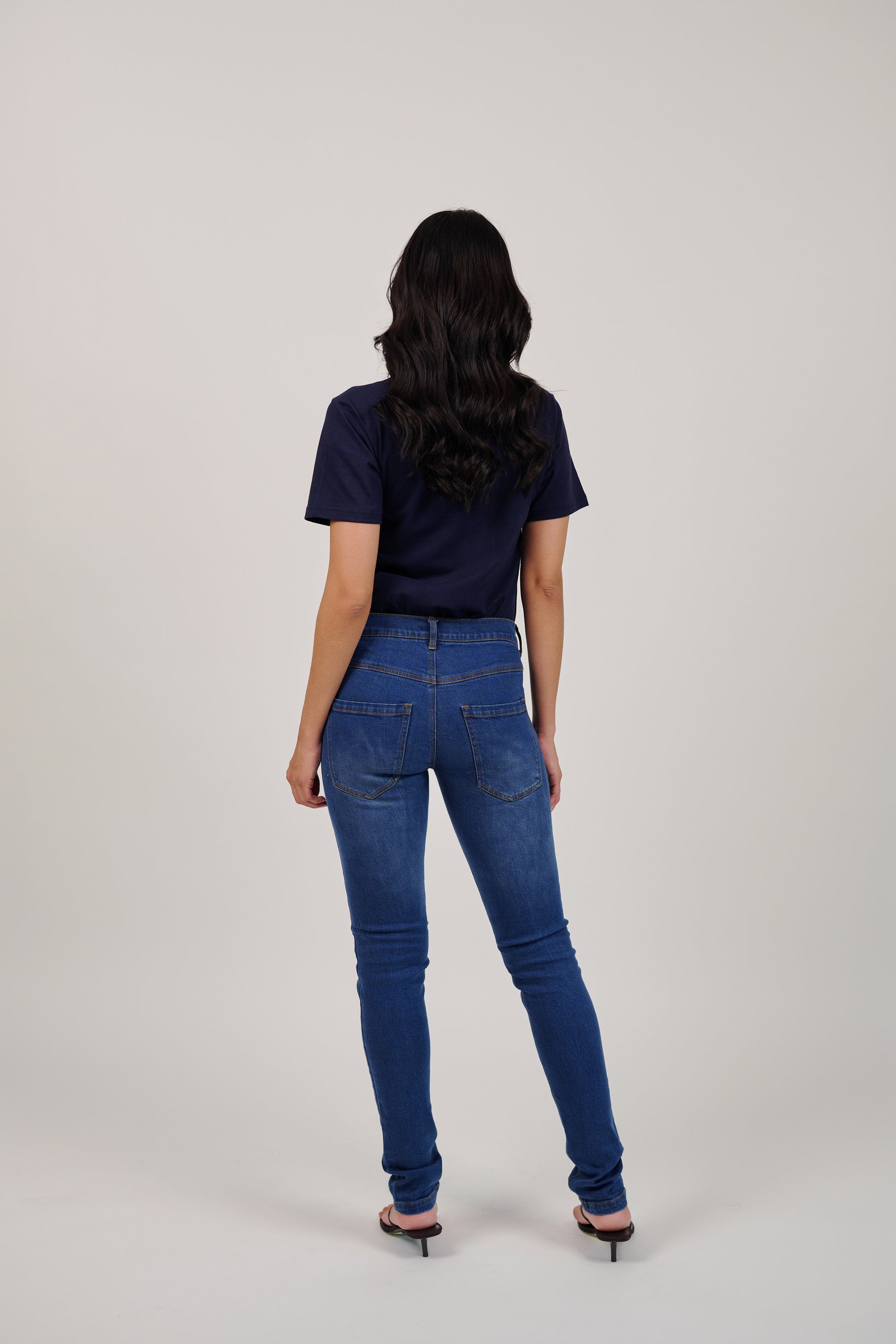 Person wearing blue jeans and a dark top on a plain background