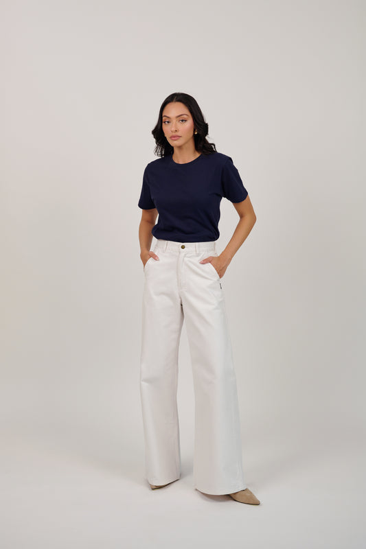 Woman wearing a navy shirt and white pants on a plain background