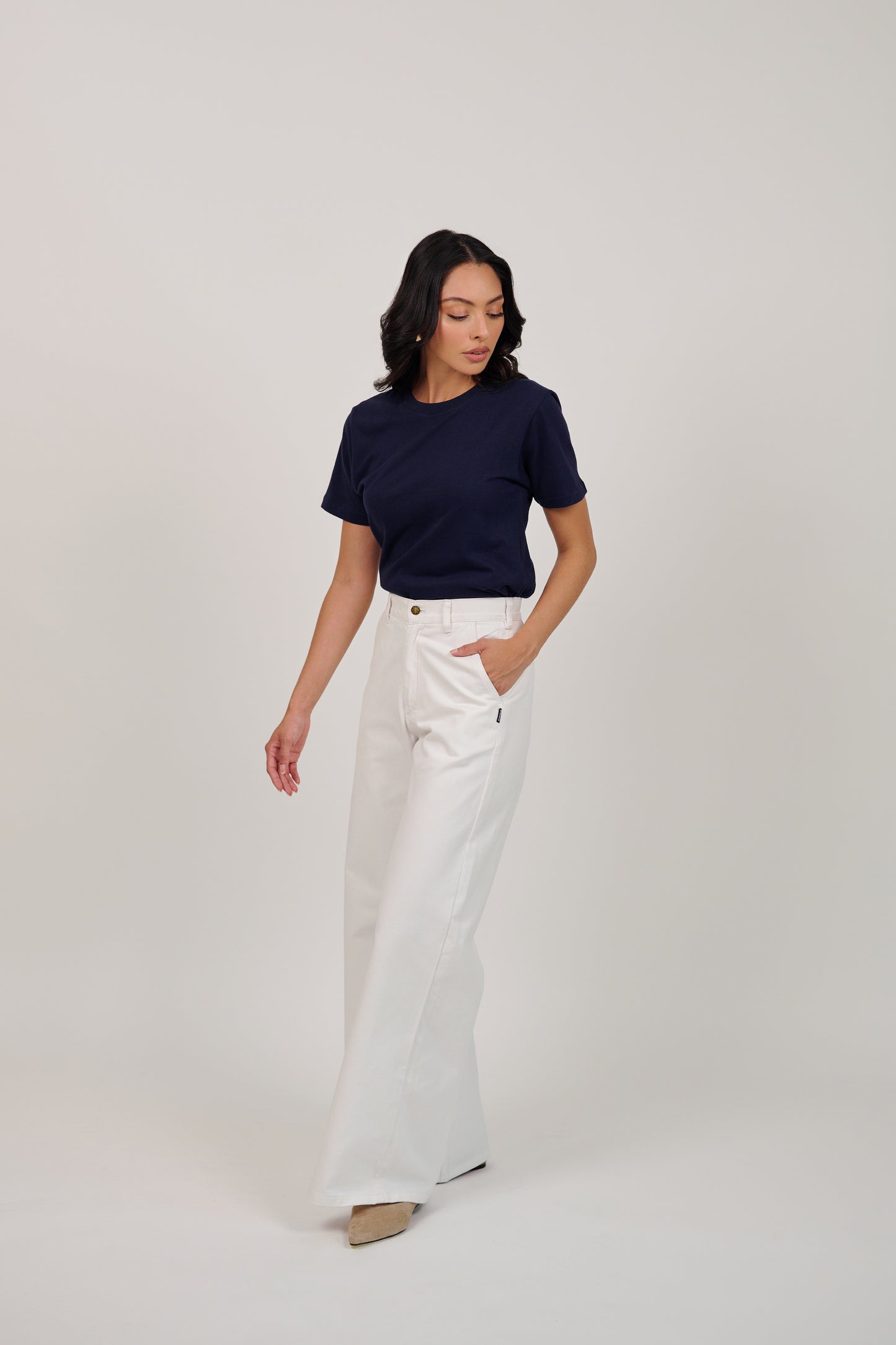 Woman wearing a navy top and white pants on a plain background