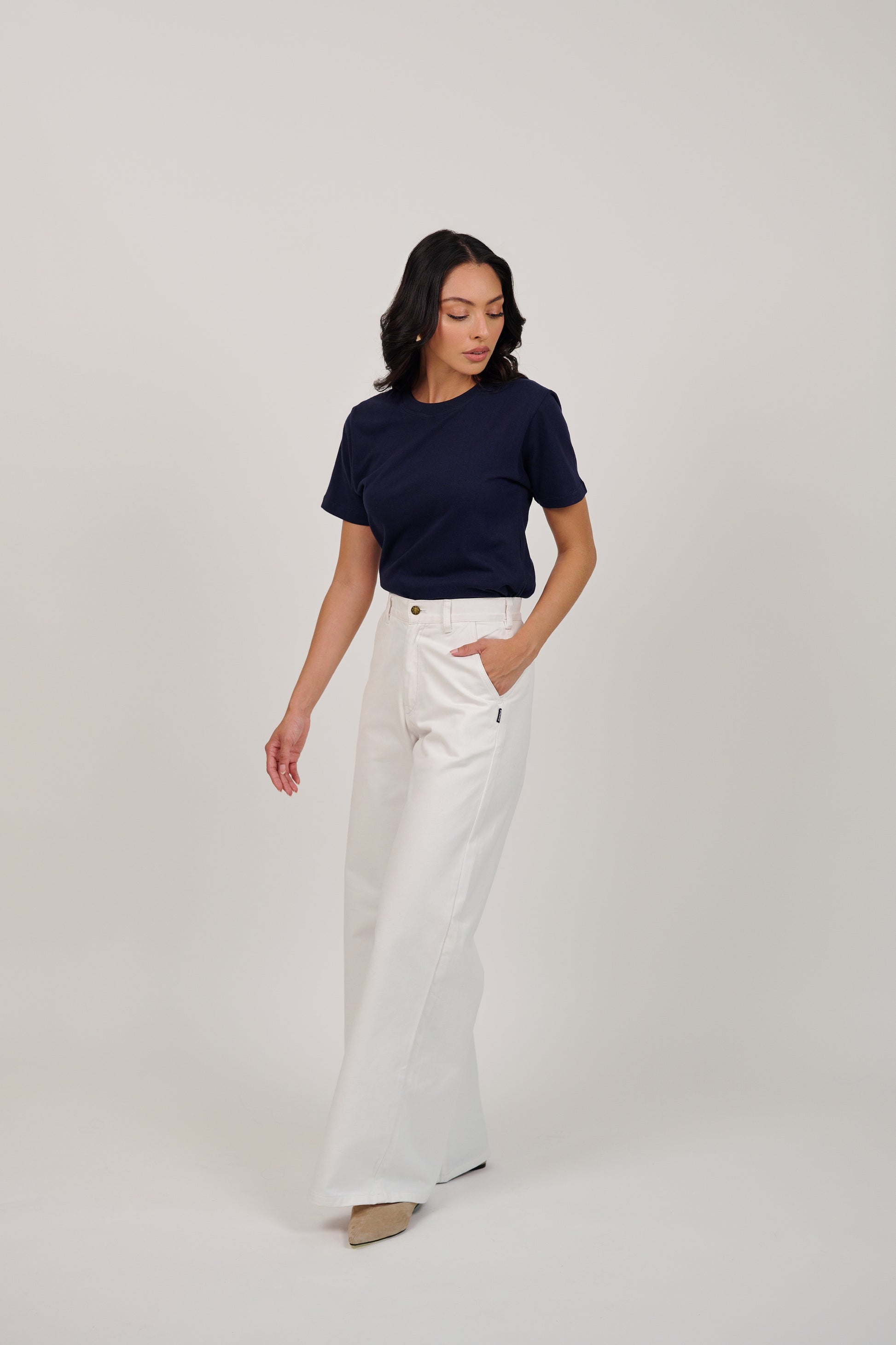 Woman wearing a navy top and white pants on a plain background