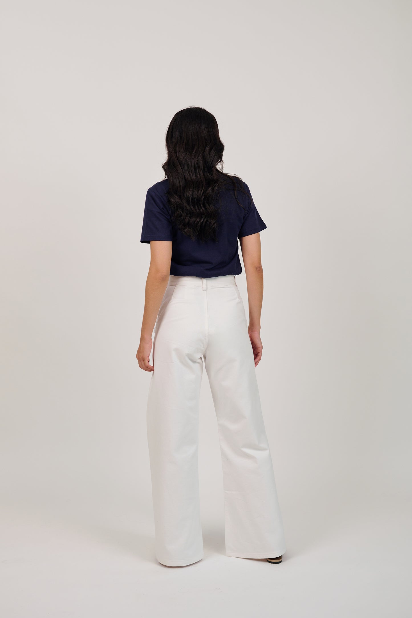 Person wearing a navy top and white pants on a plain background