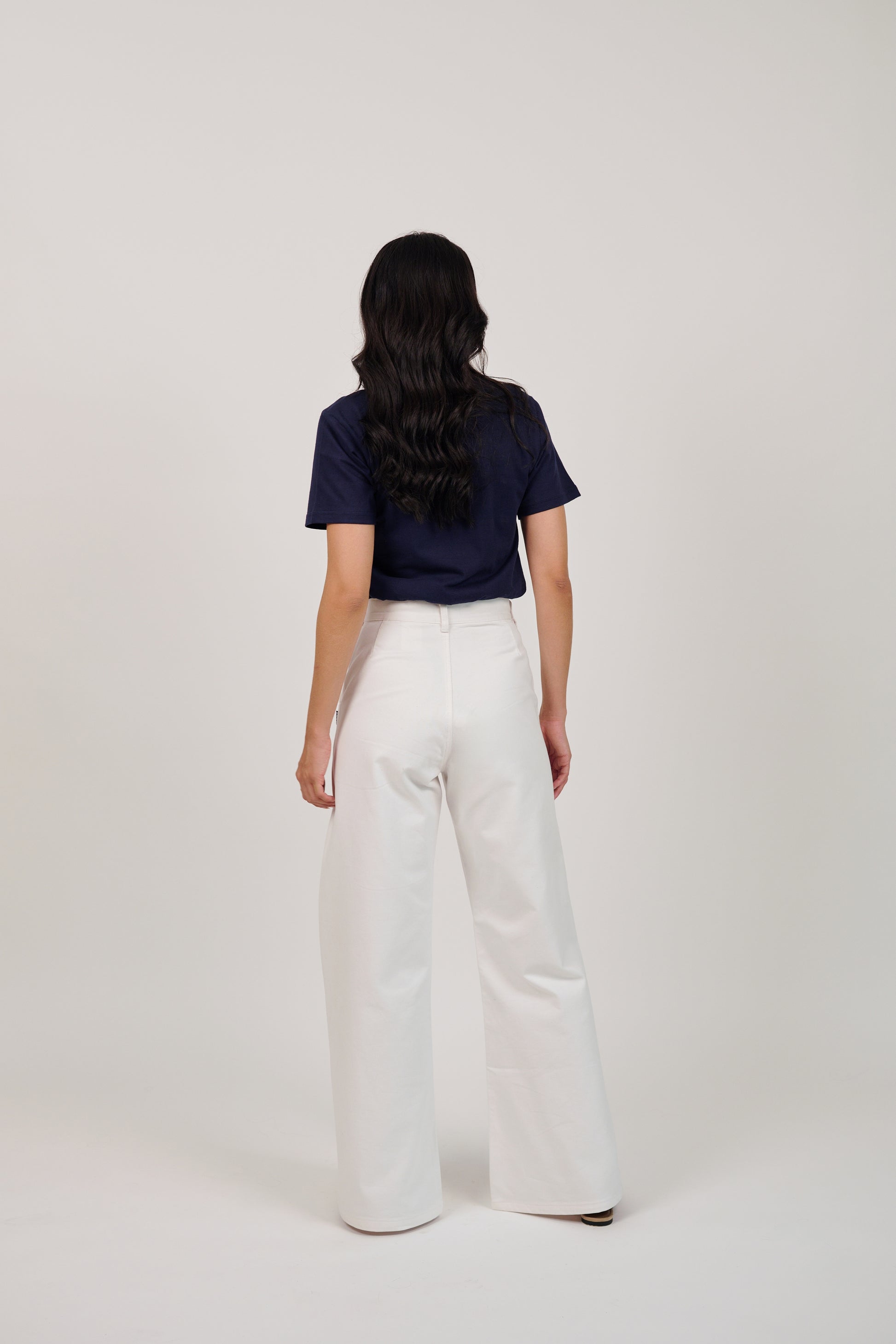 Person wearing a navy top and white pants on a plain background