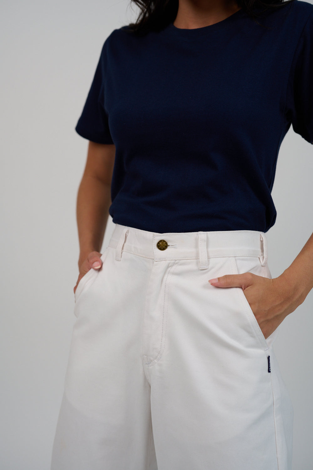 Person wearing a navy blue t-shirt and white pants against a plain background