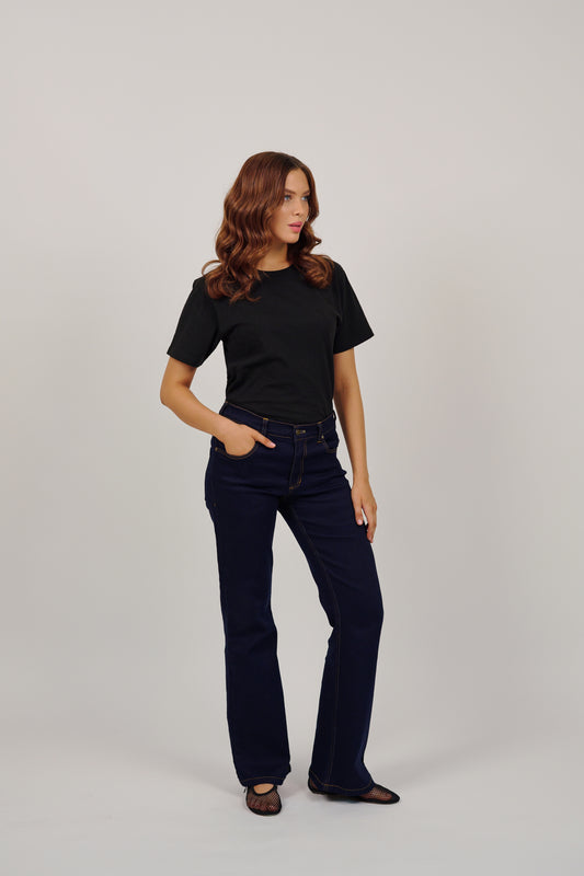 Woman wearing a black t-shirt and dark jeans on a plain background