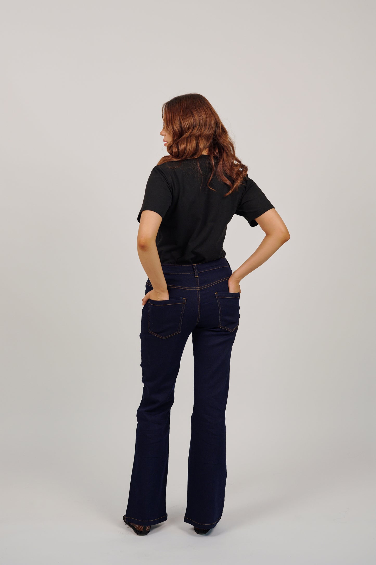 Person wearing dark blue flared jeans and a black top on a light gray background