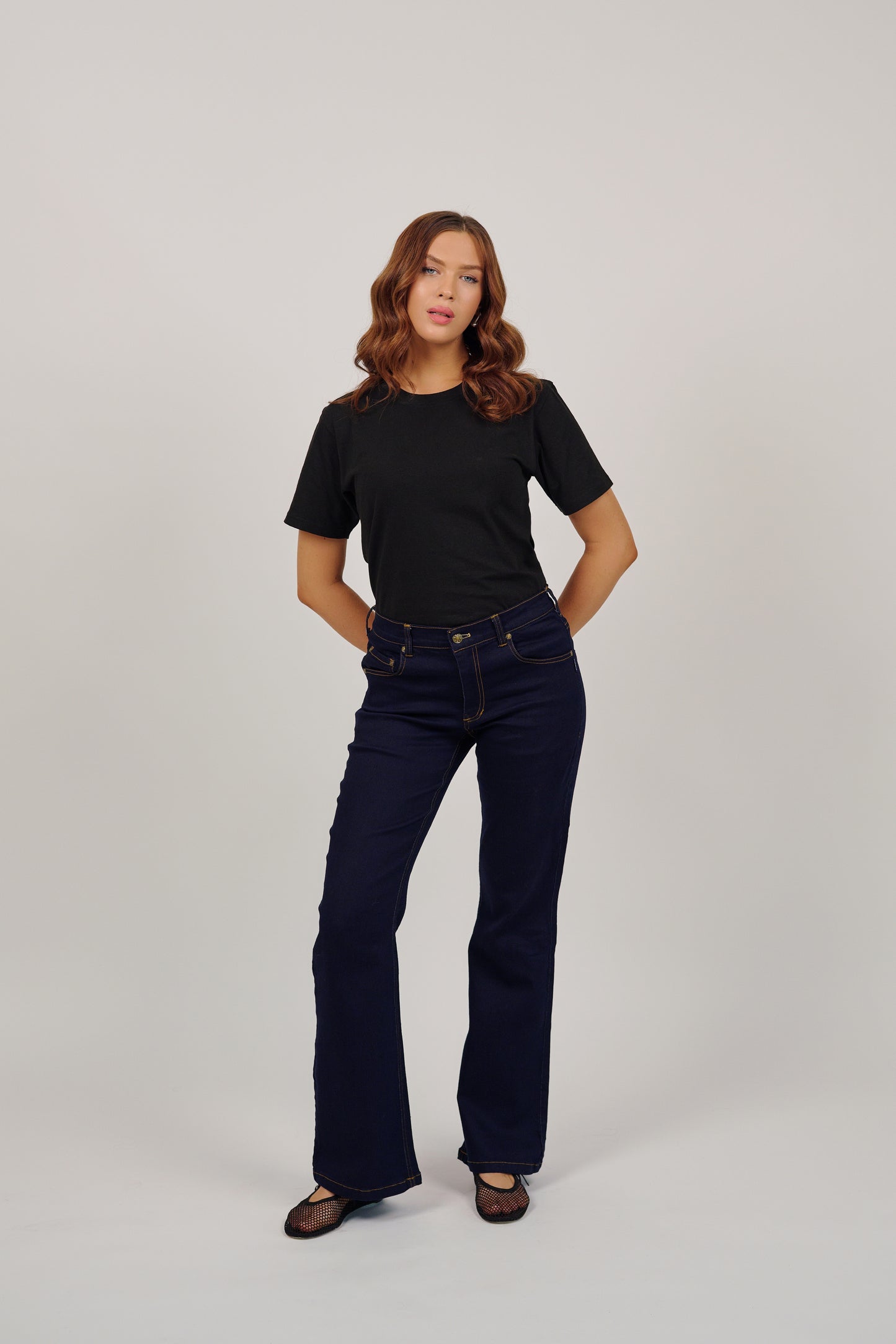 Woman wearing a black t-shirt and dark blue jeans on a white background