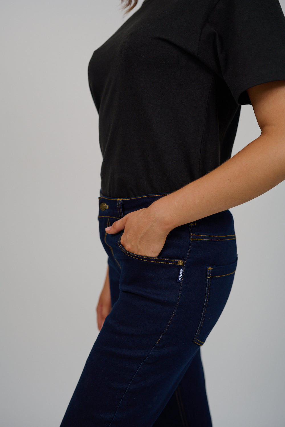 Person wearing a black t-shirt and dark blue jeans against a gray background