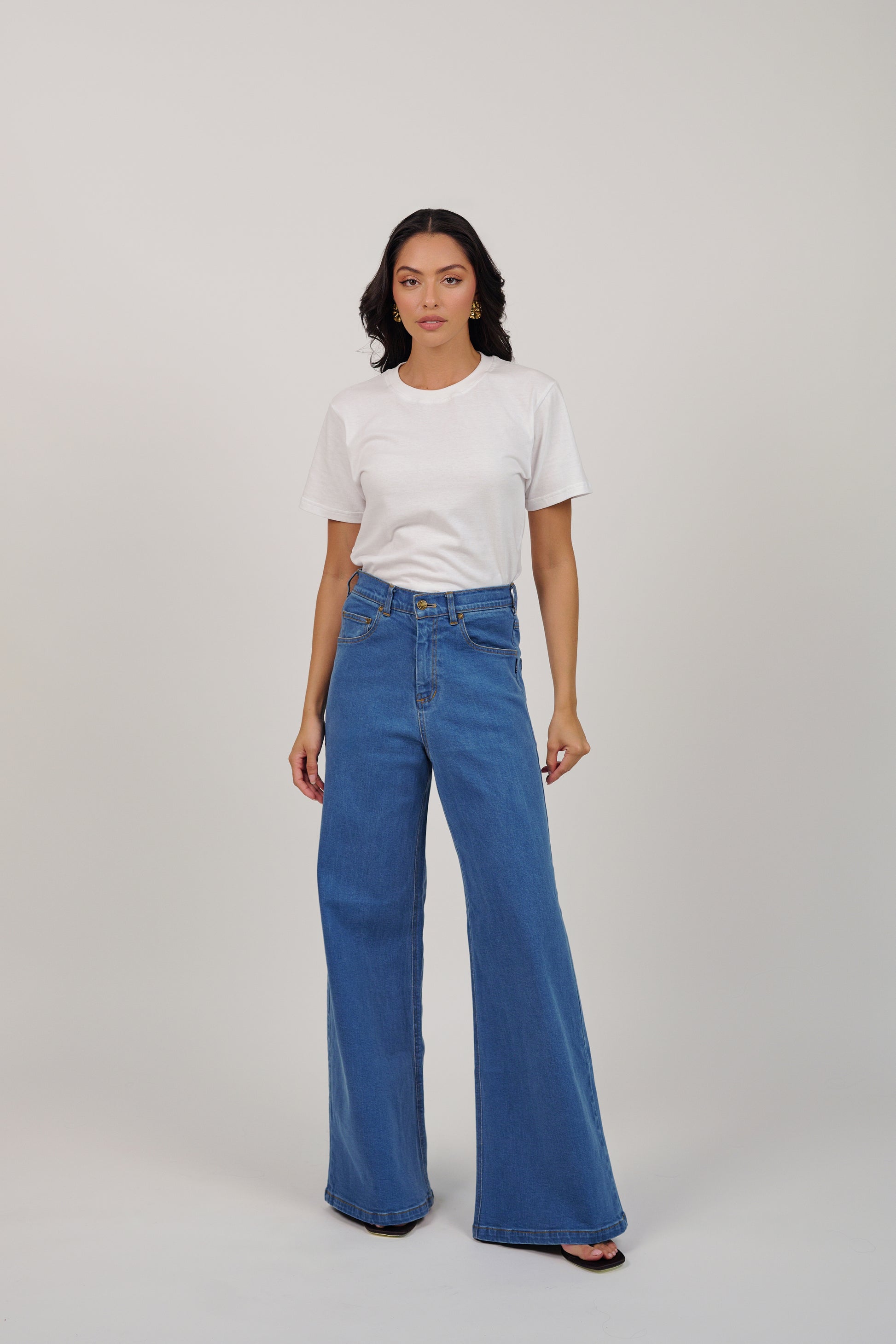 Woman wearing a white t-shirt and blue jeans on a plain background