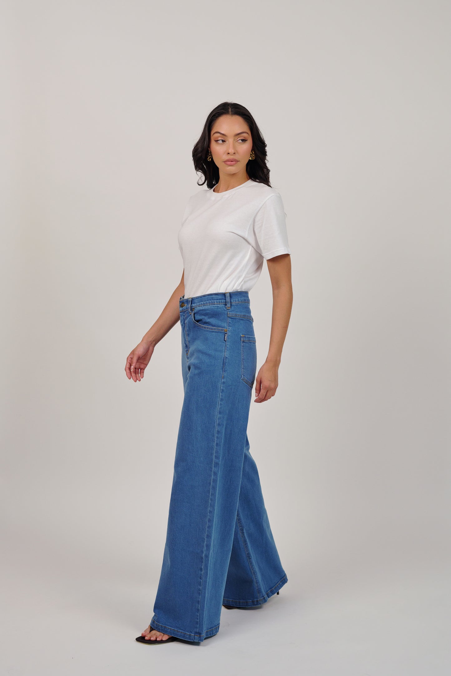Woman wearing a white t-shirt and blue flared jeans on a plain background