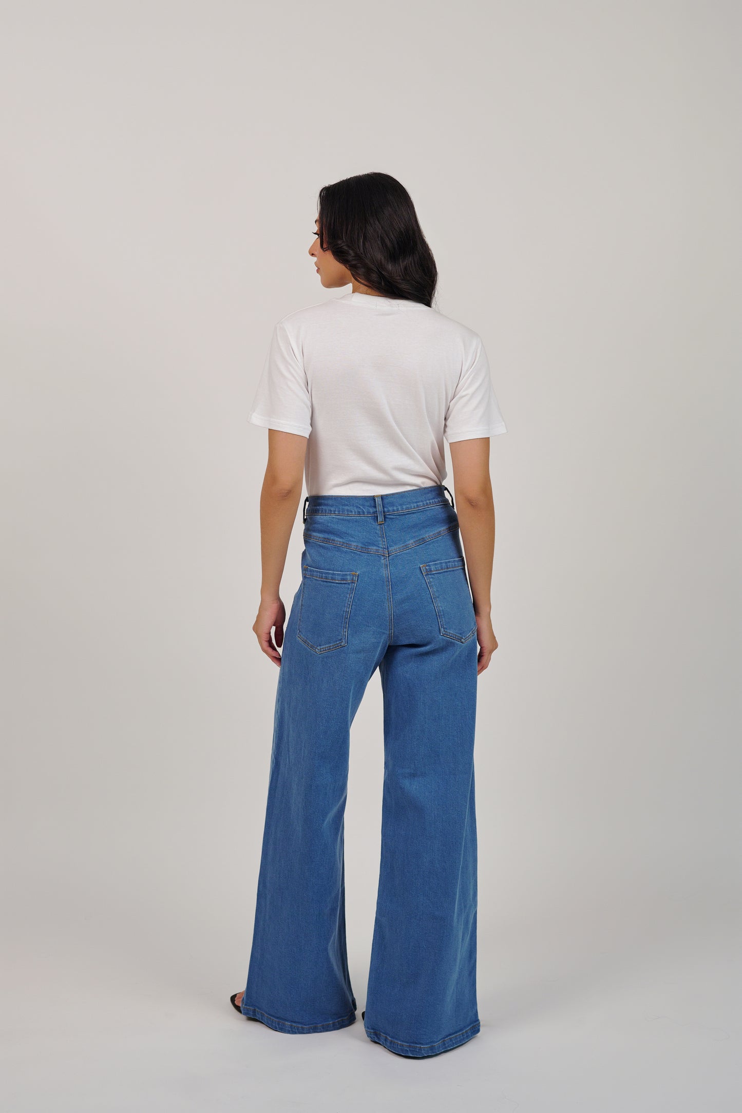 Person wearing blue jeans and a white shirt on a plain background